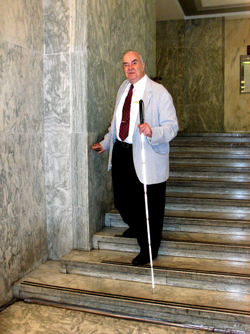 3 photos show Oral Miller wearing a suit and tie walking down a wide marble staircase.  His hand is on the end of the railing and there are still 3 steps ahead of him before he reaches the bottom.